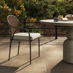 This outdoor dining chair takes inspiration from classic French bistro-style chairs, featuring a distinctive metal collar detail on the arms. The woven seatback comes together in a diamond pattern, finished with a cream-colored seat cushion. Cover or store inside during inclement weather and when not in use. Amethyst Home provides interior design, new home construction design consulting, vintage area rugs, and lighting in the San Diego metro area.