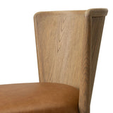 The barrel back dining chair, refreshed. Light oak shapes an armless frame and curved rear legs that almost appear to flow into the seat back. A comfy seat is upholstered in chestnut top-grain leather, while reeding details on the back create a sense of perception play. Amethyst Home provides interior design, new home construction design consulting, vintage area rugs, and lighting in the Austin metro area.