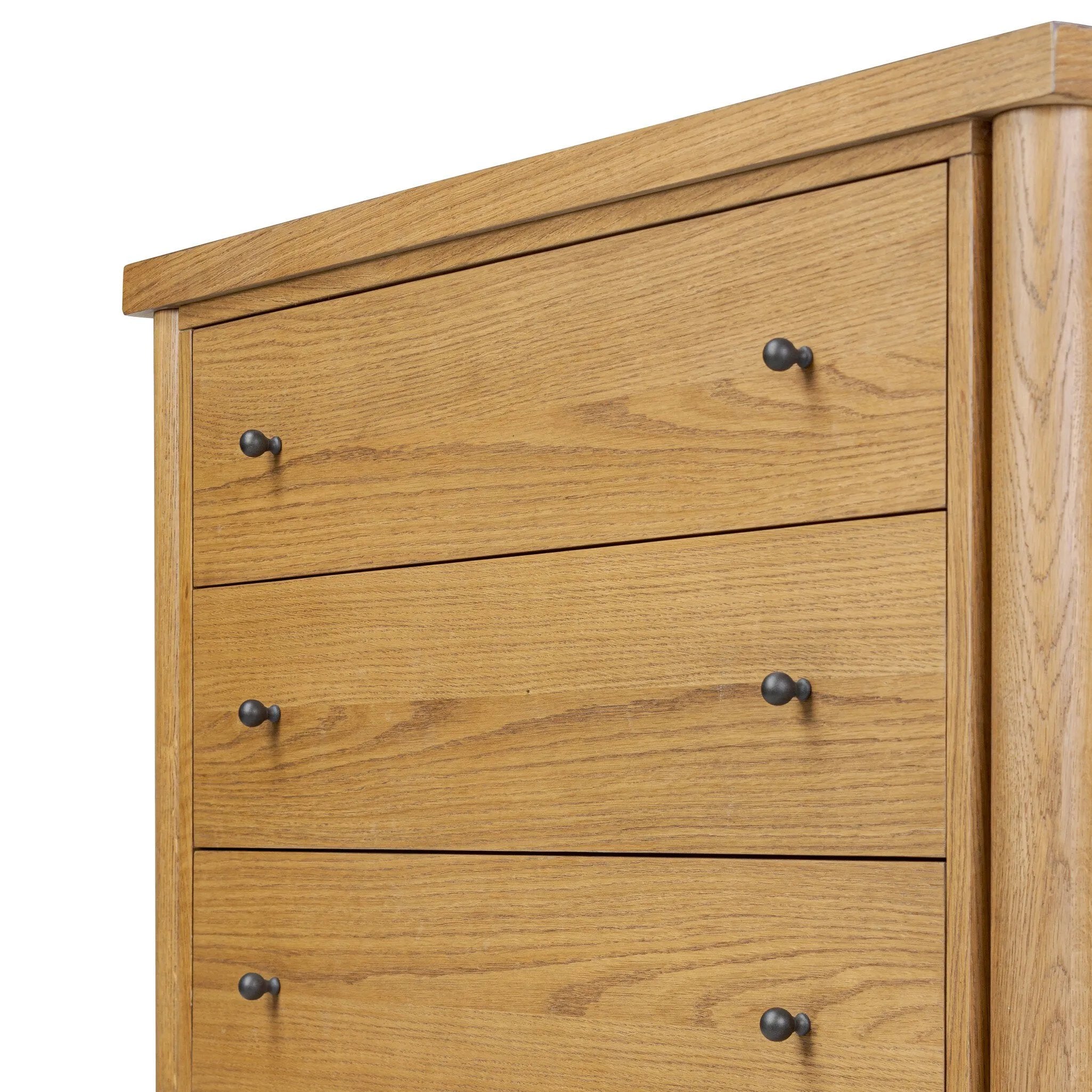 Create storage space in the bedroom with a five-drawer dresser of amber-finished oak. Chunky dowel legs support a tall silhouette and overhang top, all finished out with simple gunmetal hardware Amethyst Home provides interior design, new home construction design consulting, vintage area rugs, and lighting in the Dallas metro area.