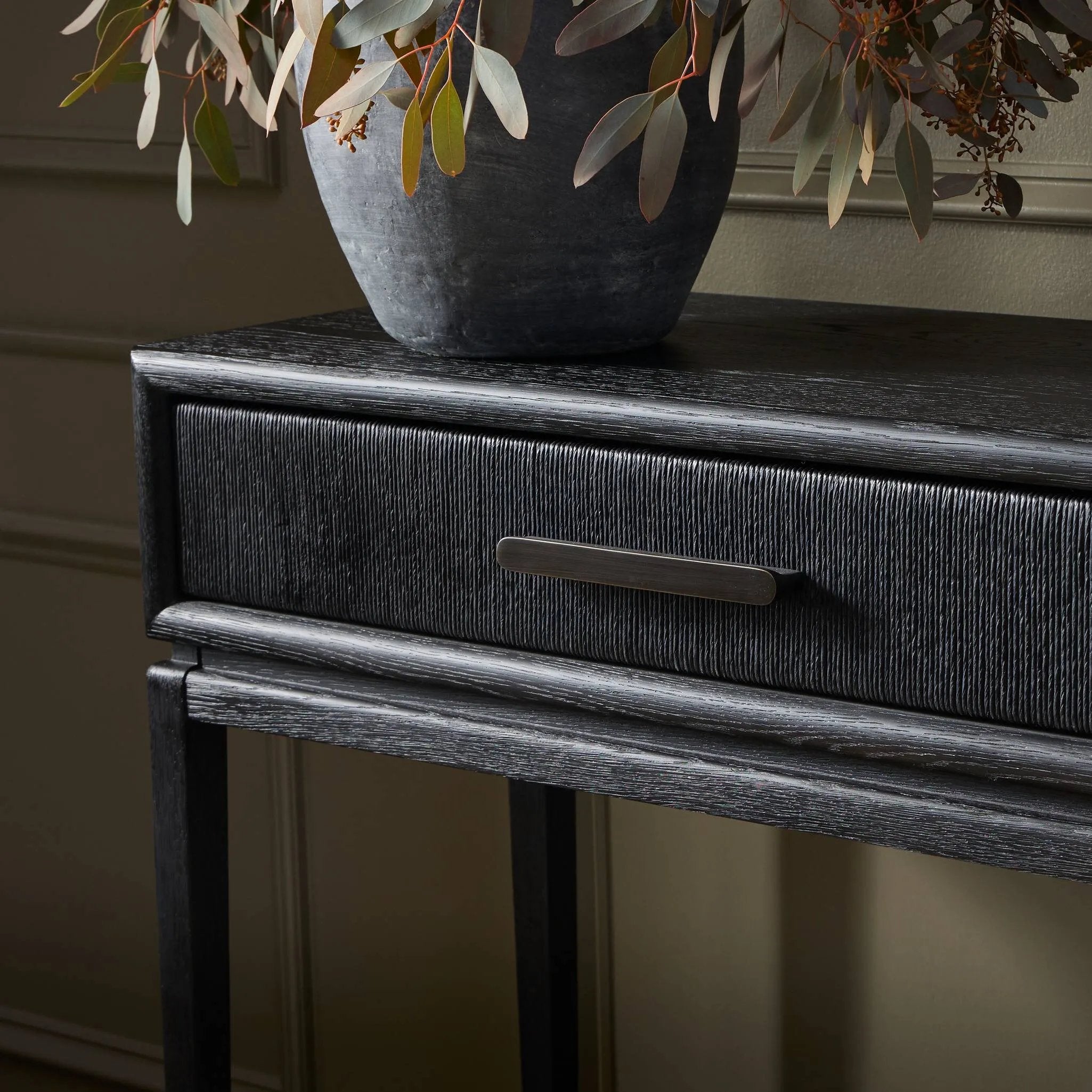 Elevate your living space or media room with a slim-profile console of black-finished oak. A smooth top pairs with two drawers covered with woven paper cord, while lower open shelving creates bonus storage and display options. The result: a dark, Scandinavian-inspired look that will work into your collection beautifully. Amethyst Home provides interior design, new home construction design consulting, vintage area rugs, and lighting in the Washington metro area.