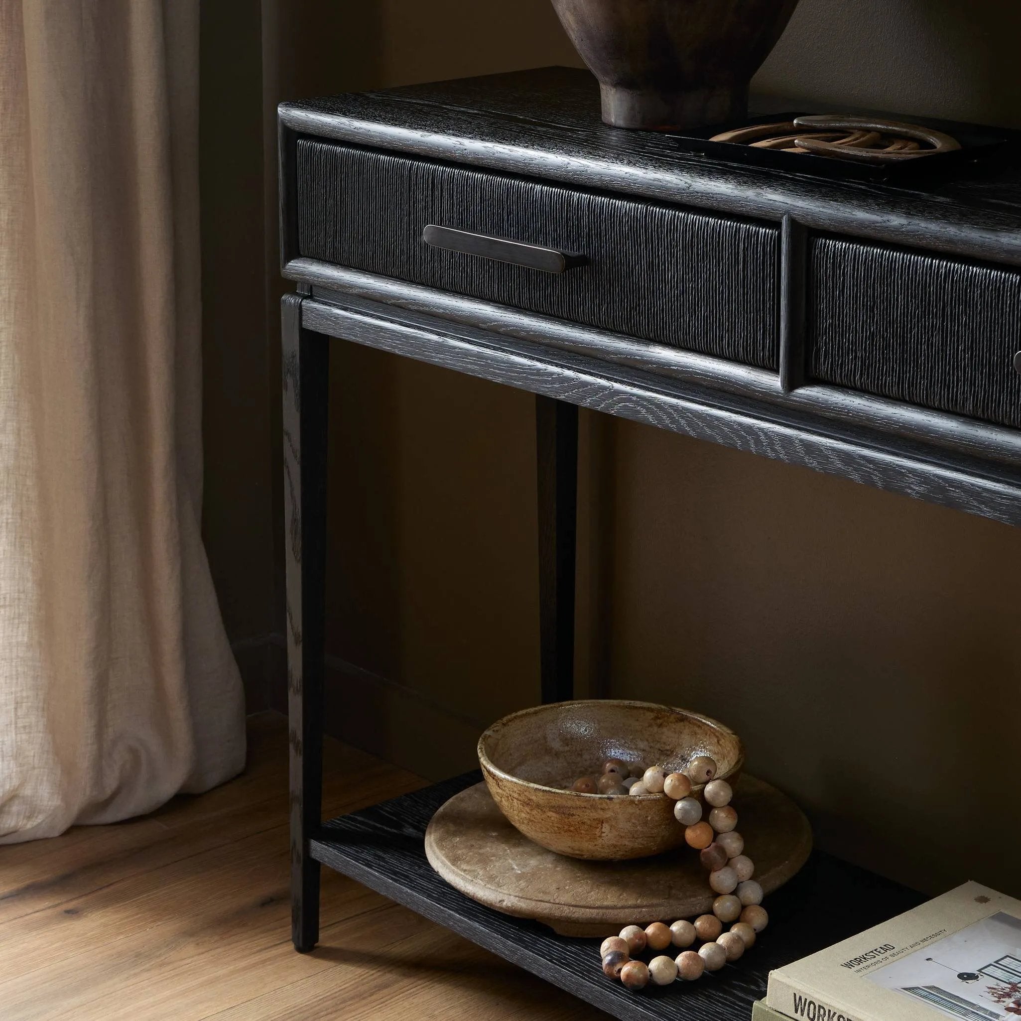 Elevate your living space or media room with a slim-profile console of black-finished oak. A smooth top pairs with three drawers covered with woven paper cord, while lower open shelving creates bonus storage and display options. The result: a dark, Scandinavian-inspired look that will work into your collection beautifully Amethyst Home provides interior design, new home construction design consulting, vintage area rugs, and lighting in the Winter Garden metro area.