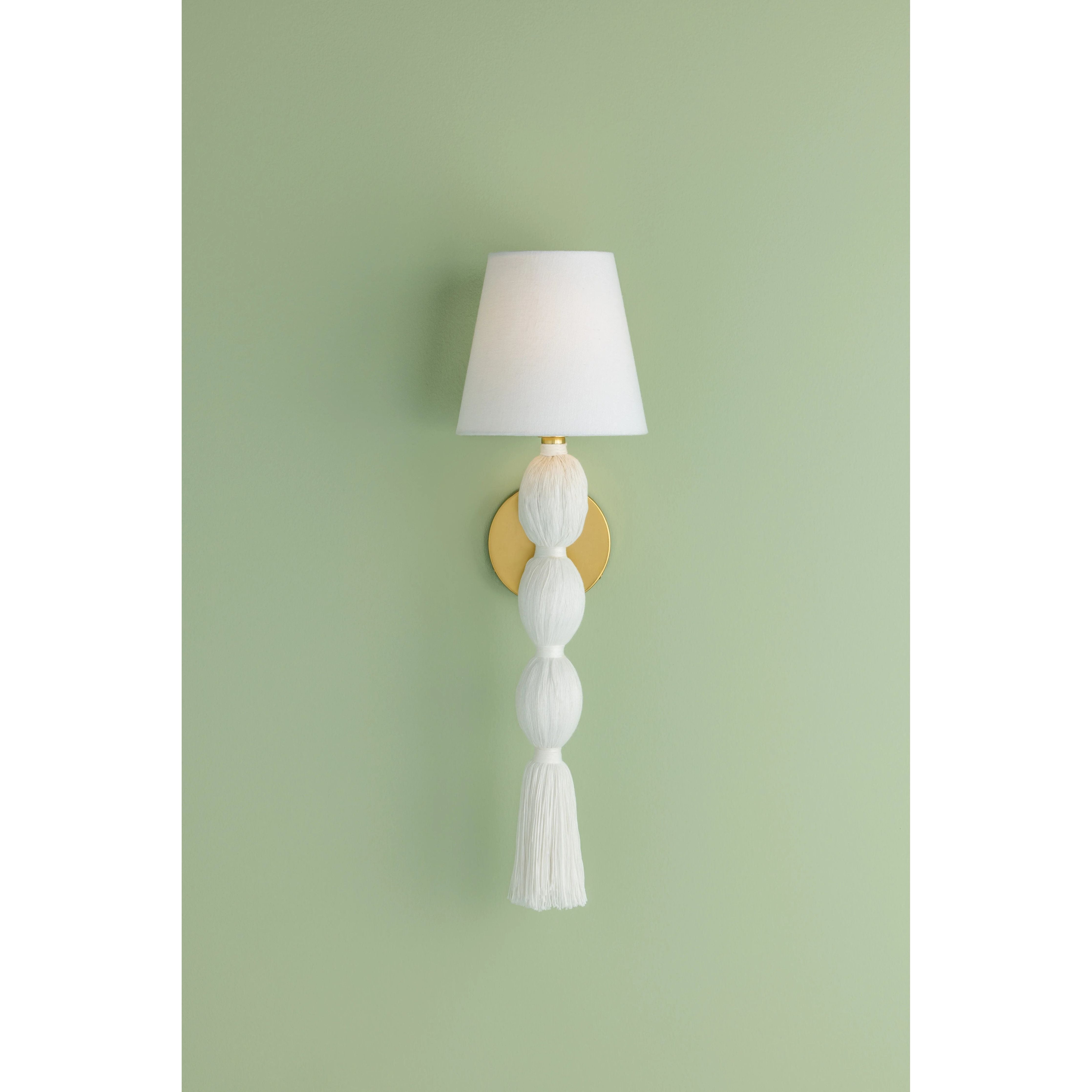 A celebration of authentic handicraft, the cinched silhouette of Indra resembles an elongated tassel. The cotton string and white linen shade create an all-over light, fresh appearance, accented by Aged Brass hardware at the neck. This single-light sconce serves as an artistic piece for small spaces in need of a spruce. Amethyst Home provides interior design, new home construction design consulting, vintage area rugs, and lighting in the Des Moines metro area.