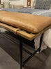 Airy, black-finished iron legs support a nettlewood dining bench of a chic, comfy layer of brandy top-grain leather on this Gabine Accent Bench - Brandy. A handsome piece to add to any bedroom, living room, or entryway.   Overall Dimensions: 72.00"w x 18.00"d x 22.00"h