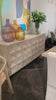 We love the textures found on this Montero Sideboard.  A wash of white and a light distressing add a whisper of color and texture to enhance this striking sideboard’s finish.   RECYCLED PINE ON IRON BASE GREY WHITE WASH FINISH Size: 84"l x 19"d x 37"h