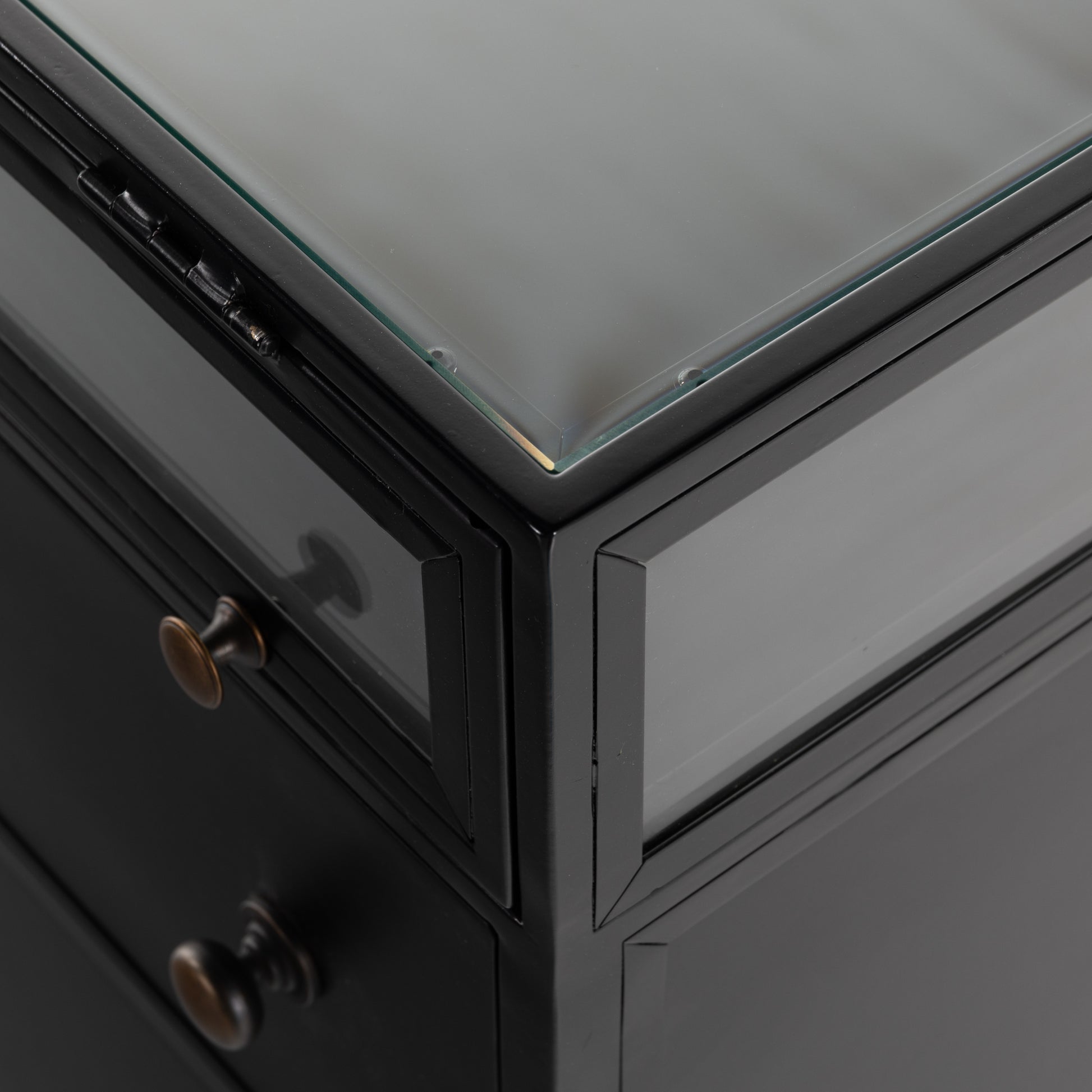 This Shadow Box Nightstand is finished in a gorgeous matte black. We love that the glass top allows you to showcase your favorite jewelry or family keepsake, while the two spacious drawers give you storage space. The knobs are finished in bronze to give this piece a sleek contrast.  Overall Dimensions: 28.00"w x 17.75"d x 30.00"h Materials: Iron, Tempered Glass, Glass