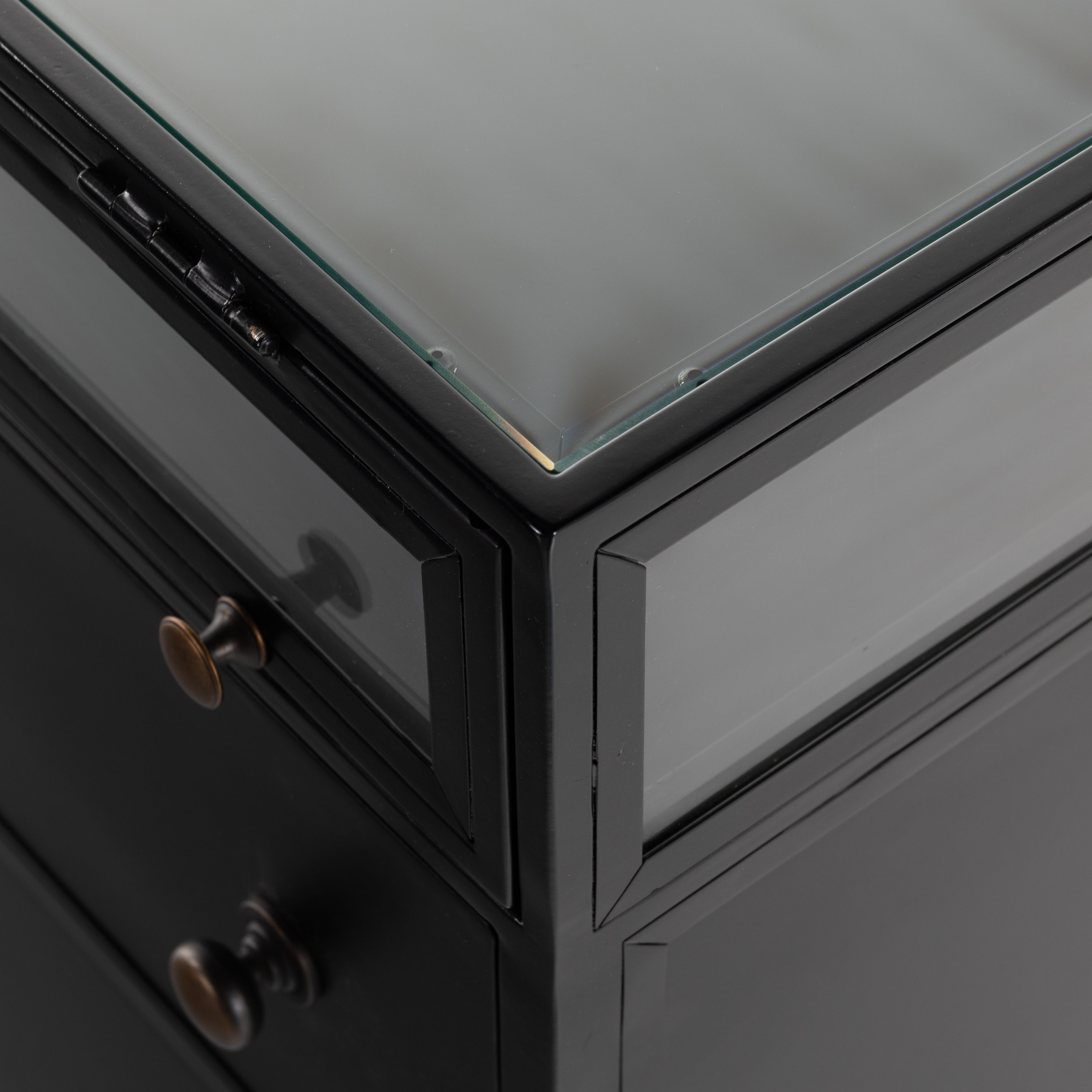 This Shadow Box Nightstand is finished in a gorgeous matte black. We love that the glass top allows you to showcase your favorite jewelry or family keepsake, while the two spacious drawers give you storage space. The knobs are finished in bronze to give this piece a sleek contrast.  Overall Dimensions: 28.00"w x 17.75"d x 30.00"h Materials: Iron, Tempered Glass, Glass