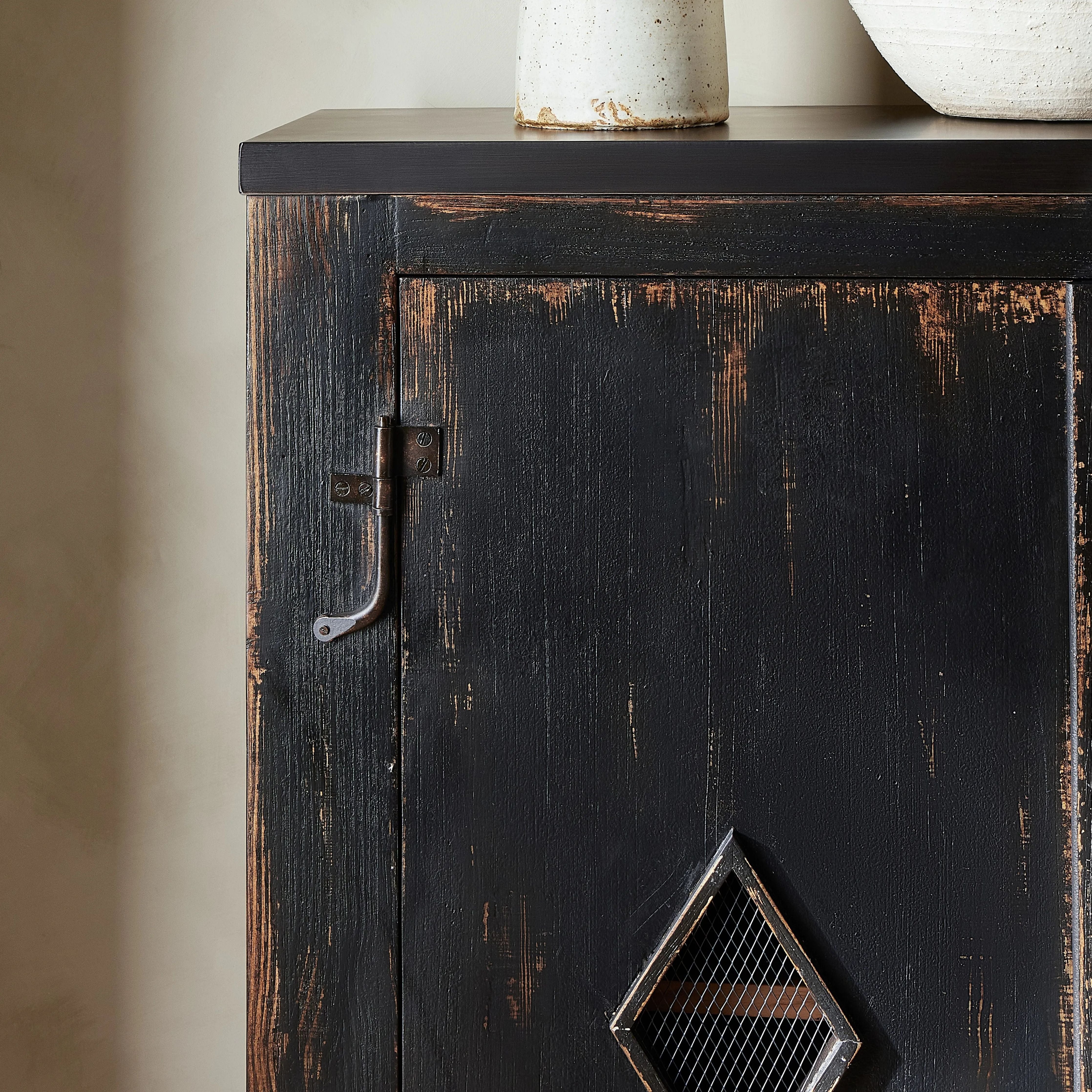 By the makers at Van Thiel, known for their antique-inspired pieces and hand-applied finishes.  This wide but slim solid pine cabinet features door fronts with diamond cutout details and wire mesh inserts. Detailed with antique-inspired hardware and hinges. Metal-clad top in oil-rubbed bronze finish. Amethyst Home provides interior design, new home construction design consulting, vintage area rugs, and lighting in the Tampa metro area.